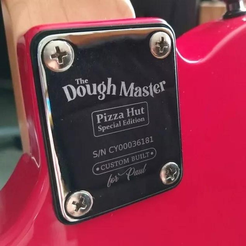 May include: A black plate with silver screws, attached to a red surface. The plate reads "The Dough Master" and "Pizza Hut Special Edition." The serial number and "Custom Built for Paul" are also visible.