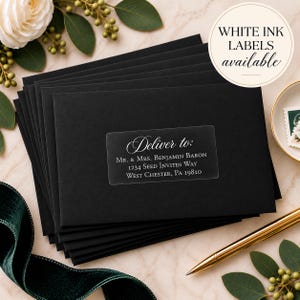 Pu&ograve; includere: Una pila di buste rettangolari nere con un'etichetta adesiva trasparente per spedizioni con testo bianco che recita Deliver to: Mr. & Mrs. Benjamin Baron, 1234 Seed Invites Way, West Chester, PA 19810. Un grafico circolare indica WHITE INK LABELS available.