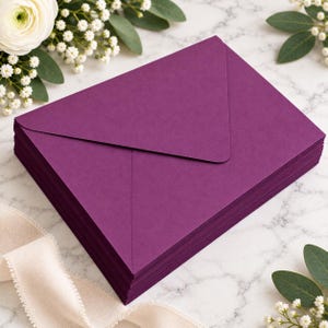 Può includere: Una pila di buste color viola intenso con un design a patta appuntita. Le buste sono rettangolari e presentano una finitura liscia e opaca. La pila è allineata in modo ordinato, mostrando il colore uniforme e la consistenza della carta.
