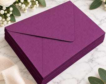 May include: A stack of deep purple envelopes with a pointed flap design. The envelopes are rectangular and feature a smooth, matte finish. The stack is neatly aligned, showing the consistent color and paper texture of each individual envelope.