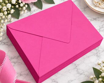 May include: A stack of vibrant hot pink envelopes with a classic triangular flap design. The envelopes are arranged in a neat pile, showcasing a smooth, matte texture and a bold, saturated color that stands out against the surrounding floral decor.