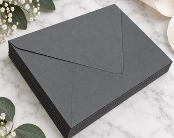 May include: A stack of rectangular dark charcoal gray envelopes with a pointed flap design. The envelopes are arranged in a neat pile, showcasing a smooth, matte paper texture and clean, sharp edges on each individual piece of stationery.