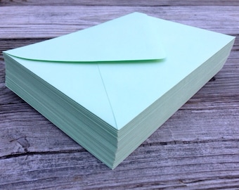 May include: A stack of light green envelopes, neatly arranged on a wooden surface.