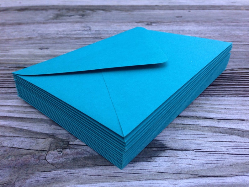 Peut inclure: Une pile d'enveloppes bleu turquoise, soigneusement dispos&eacute;es sur une surface en bois.