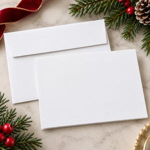 Può includere: Un biglietto d'auguri rettangolare bianco vuoto e una busta bianca abbinata. Il biglietto è posizionato davanti alla busta, entrambi caratterizzati da una finitura liscia e opaca. Il set di cancelleria si presenta con un design pulito.