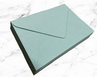 May include: A stack of light teal-colored envelopes. The envelopes are rectangular with a pointed flap and are stacked neatly on top of each other. The background is a white marble pattern.