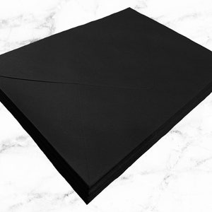 Pu&ograve; includere: Una pila di buste rettangolari nere con un design a patta a punta. Le buste sono impilate ordinatamente l'una sull'altra, mostrando una consistenza di carta nera opaca uniforme e bordi netti e puliti su tutti i lati del set di cancelleria.
