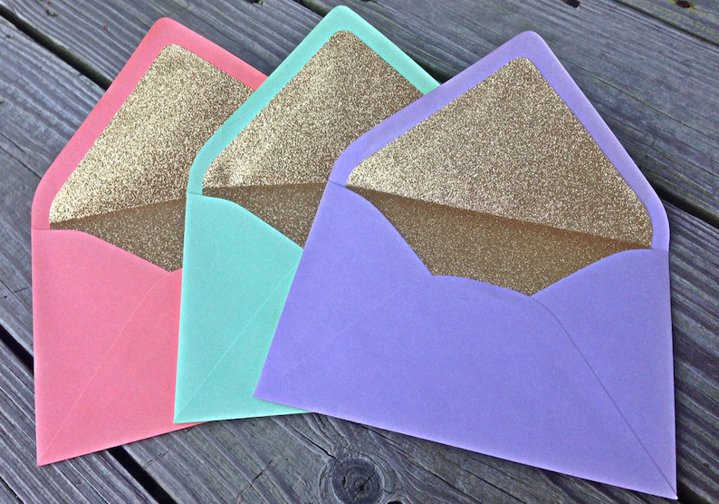 Pu&ograve; includere: Tre buste con fodera in glitter dorata. Le buste sono rosa, turchese e lavanda.