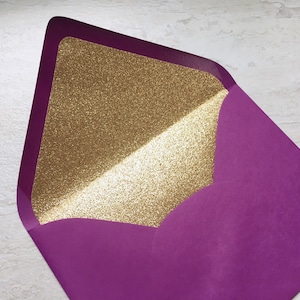 May include: A purple envelope with a gold glitter lining. The envelope is folded in half and the gold glitter lining is visible on the inside.