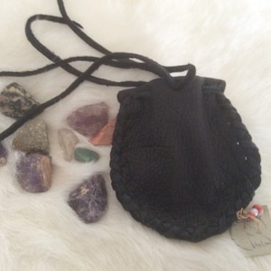 May include: A small black leather pouch with a drawstring closure and a braided edge. The pouch is surrounded by a variety of colourful stones, including amethyst, clear quartz, and green aventurine.
