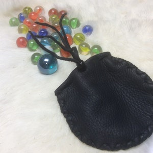 May include: A small black leather pouch with a drawstring closure. The pouch is surrounded by colorful glass marbles.