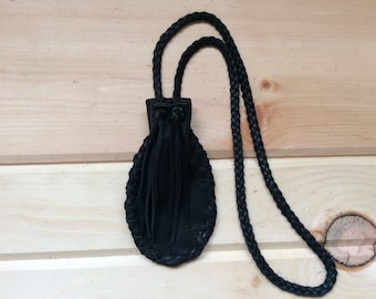 May include: A black leather pouch with a braided cord necklace. The pouch has a fringe detail and is closed with a leather tie.