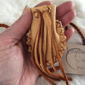 May include: A small, tan leather pouch with a braided design and long fringe. The pouch has a drawstring closure and a braided cord. A tag reads "Leather by Lisa".