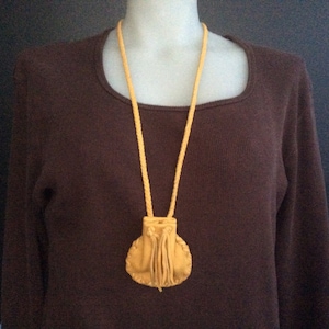 May include: A yellow leather pouch with a drawstring closure hangs from a yellow leather cord. The pouch is worn as a necklace.