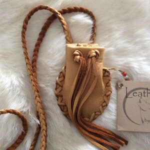 May include: A small, tan leather pouch with a braided strap and decorative fringe. The pouch features woven detailing and a drawstring closure. A tag with the text "Leather by Lisa" is attached.