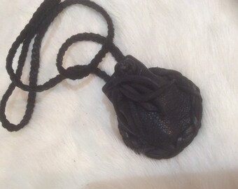 May include: A black leather pouch with a braided cord. The pouch is closed with a drawstring and has a decorative stitch around the edge.
