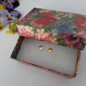 May include: A pair of small, gold-colored earrings in a floral patterned gift box.