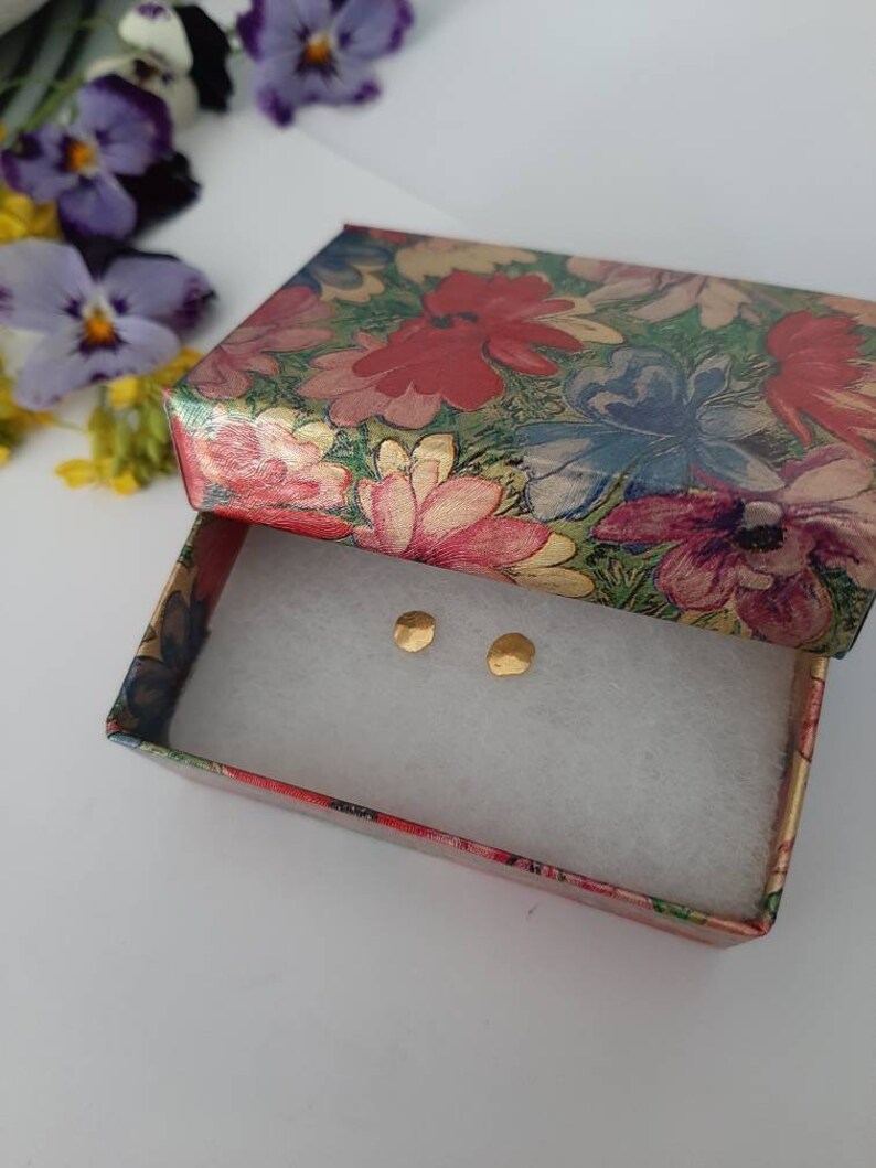 May include: A pair of small, gold-colored earrings in a floral patterned gift box.