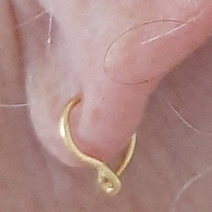 Pu&ograve; includere: Un orecchino a cerchio d'oro con un designo unico a torsione. L'orecchino &egrave; indossato sul lobo dell'orecchio.