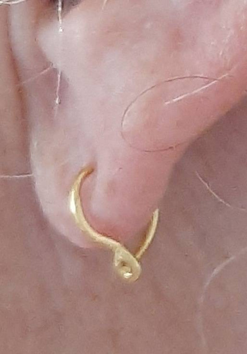 Pu&ograve; includere: Un orecchino a cerchio d'oro con un designo unico a torsione. L'orecchino &egrave; indossato sul lobo dell'orecchio.