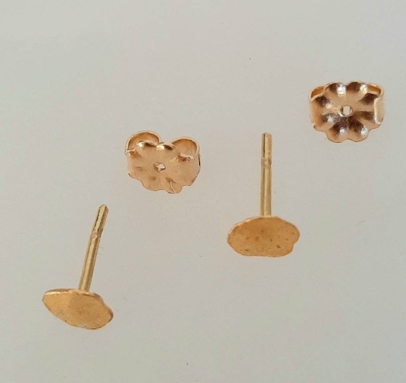 May include: Three gold-toned earring backs, two are round and one is a flower shape.
