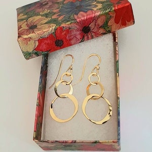 May include: A pair of gold dangle earrings with multiple interlocking circles. The earrings are in a floral patterned gift box.