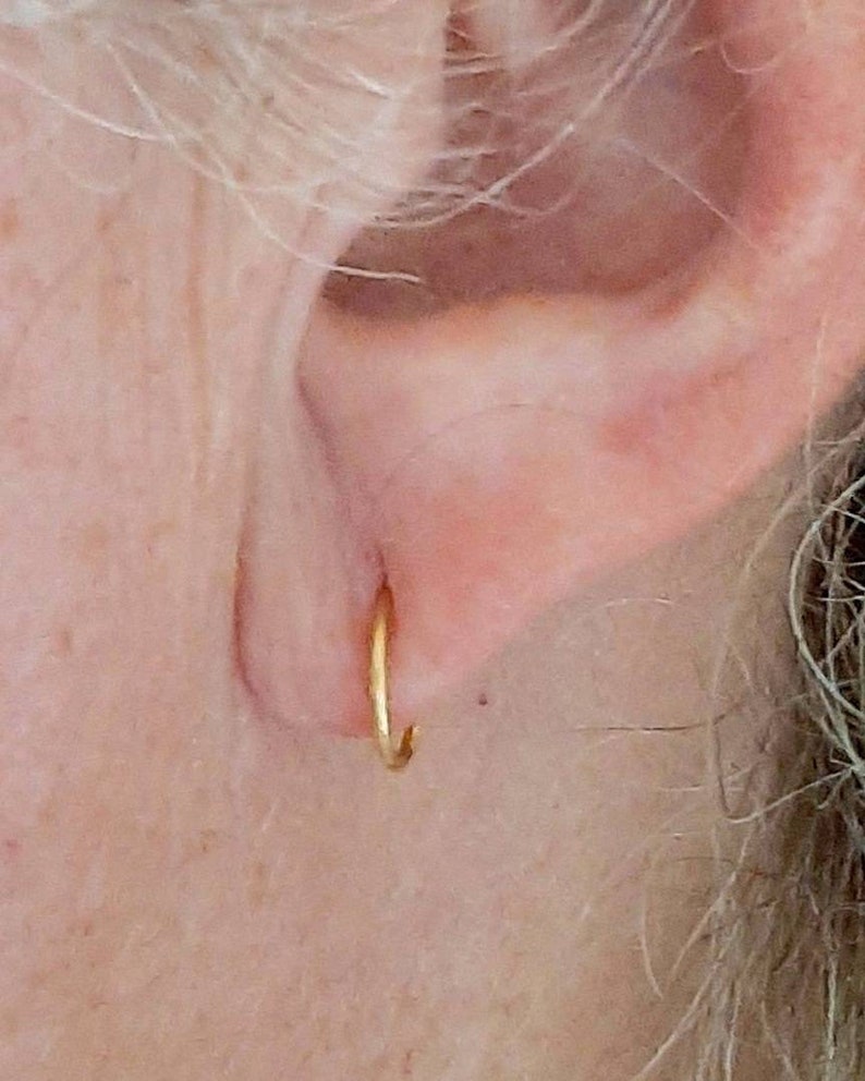 Pu&ograve; includere: Primo piano di un orecchio con un piccolo orecchino a cerchio d'oro.