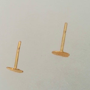 May include: A pair of gold stud earrings with a round shape. The earrings are simple and elegant.