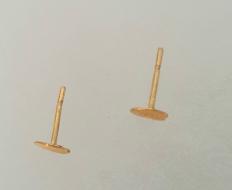 May include: A pair of gold stud earrings with a round shape. The earrings are simple and elegant.