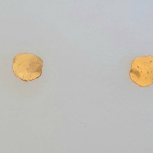 May include: Two small, irregularly shaped, gold-colored metal pieces on a white background.
