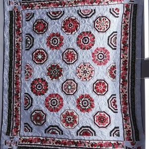May include: A quilt with a blue background and a pattern of red and white flowers. The quilt is edged with a border of green, red, and white floral fabric.