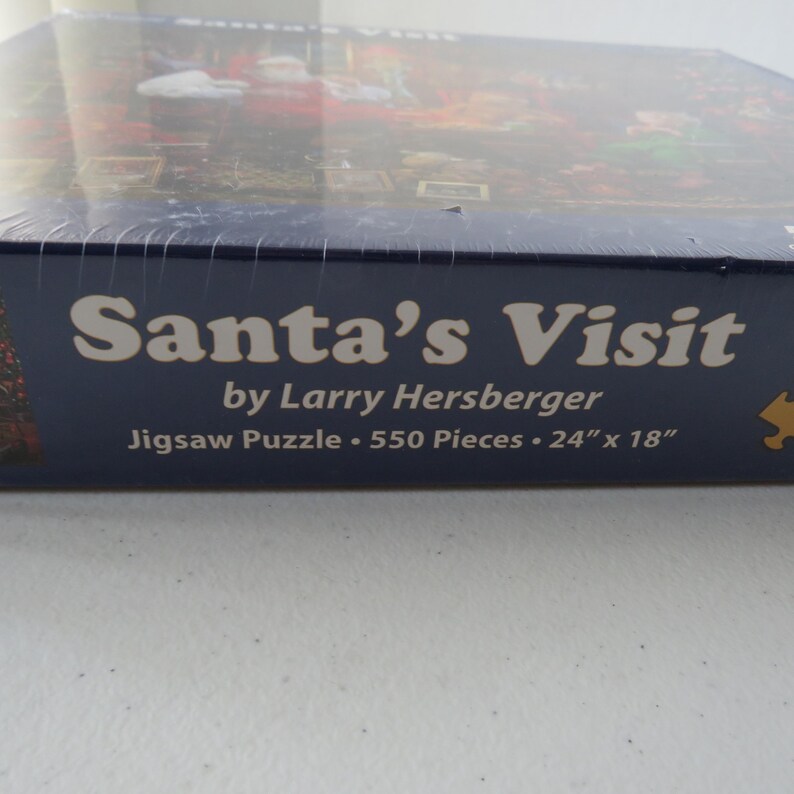 May include: A boxed jigsaw puzzle titled "Santa's Visit" by Larry Hersberger. The box is dark blue with white text. The puzzle contains 550 pieces and measures 24 inches by 18 inches.