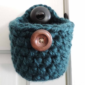May include: A teal crocheted hanging basket with a wooden button and a black plastic hook.