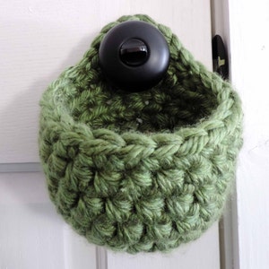 May include: A green crocheted hanging basket with a black button on the top.