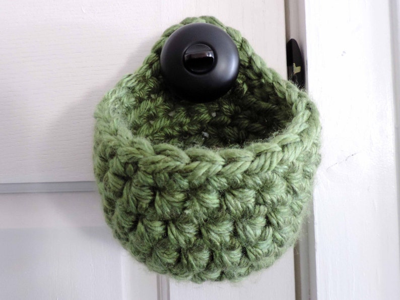 May include: A green crocheted hanging basket with a black button on the top.