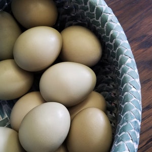 May include: A basket filled with a dozen light brown eggs. The basket is woven with a green and white pattern.