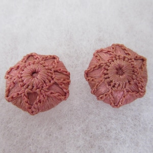 May include: Two handmade, dusky pink embroidered buttons. Each button features a central circular design surrounded by a detailed, geometric pattern. The buttons are set against a white, textured background.