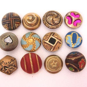 May include: A selection of twelve antique buttons in diverse designs. The buttons display colours such as gold, red, blue, and pink, with detailed patterns and textures. Some have floral, geometric, and star motifs.