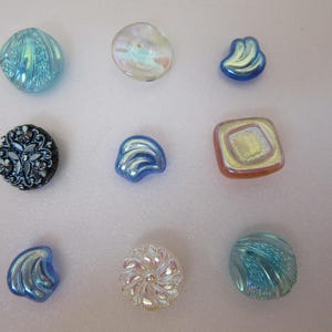 May include: A selection of iridescent glass buttons in various shapes and sizes. The buttons feature shades of blue, white, and iridescent colours. Some have textured surfaces, while others are smooth. These decorative buttons are ideal for sewing and craft projects.