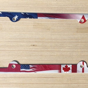 May include: A white metal license plate frame with a design of the American and Canadian flags. The flags are red, white, and blue.