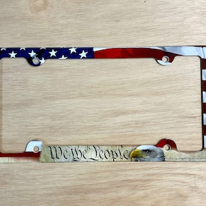 May include: License plate frame featuring the American flag design with stars and stripes. The frame includes the text "We the People" and an image of an eagle. The frame is designed to fit a standard U.S. license plate.