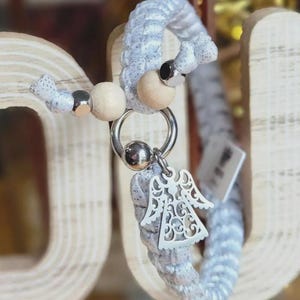 Puede incluir: Un llavero trenzado plateado y blanco con un dije decorativo de &aacute;ngel. El llavero presenta cuentas de madera y un anillo plateado. El dije de &aacute;ngel est&aacute; intrincadamente dise&ntilde;ado con detalles recortados.