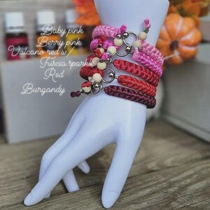 Puede incluir: Una exhibici&oacute;n de pulseras rosas y rojas, adornadas con cuentas y anillos met&aacute;licos. Las pulseras est&aacute;n apiladas en una mano blanca. El texto en la imagen dice: Baby pink, Berry pink, Volcano red w/, Fuscia sparkle, Red, Burgundy.