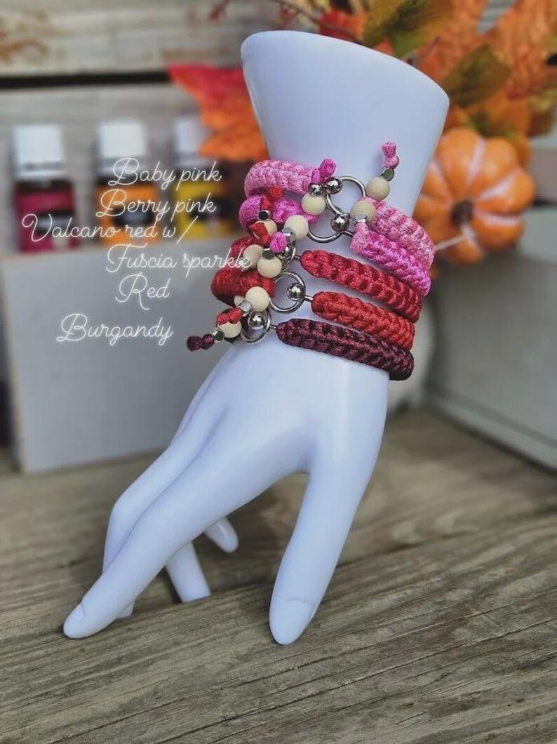 Puede incluir: Una exhibici&oacute;n de pulseras rosas y rojas, adornadas con cuentas y anillos met&aacute;licos. Las pulseras est&aacute;n apiladas en una mano blanca. El texto en la imagen dice: Baby pink, Berry pink, Volcano red w/, Fuscia sparkle, Red, Burgundy.