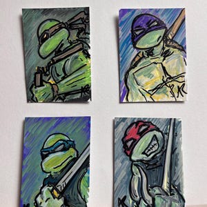 May include: Four small, colorful paintings of Teenage Mutant Ninja Turtles. Each turtle is depicted with a different colored mask: green, purple, blue, and red. The artwork has a hand-painted style with visible brushstrokes and a white background.