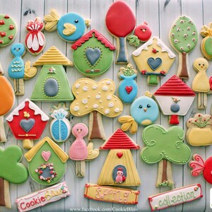 May include: A collection of decorated sugar cookies featuring birdhouses, trees, birds, and other spring-themed designs. The cookies are decorated with colorful icing and sprinkles. The text "Cookie Bliss Collection" is written on a banner at the bottom of the image.