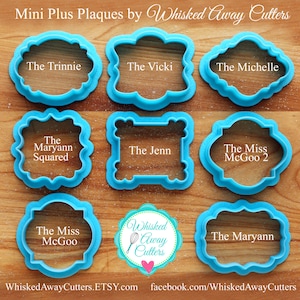 May include: Nine blue plastic cookie cutters in various shapes and sizes, with names like "The Trinnie", "The Vicki", "The Michelle", "The Maryann Squared", "The Jenn", "The Miss McGoo 2", "The Miss McGoo", and "The Maryann". The cutters are arranged on a wooden surface. The logo for "Whisked Away Cutters" is in the center of the image.