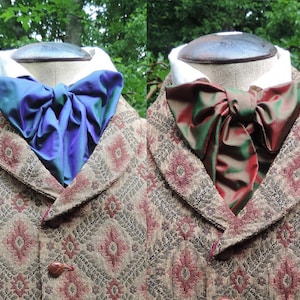 May include: Two cravats, one blue and one green and red, tied in a bow on a brown patterned jacket.