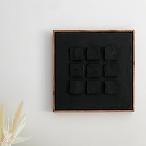 May include: A black and white abstract painting with a textured surface, framed in a dark wood frame, hangs on a white wall above a wooden table with a black candle holder and books. The books are titled "The Sun's Coming Up", "Cinema", and "Burning Man Art on Fire".
