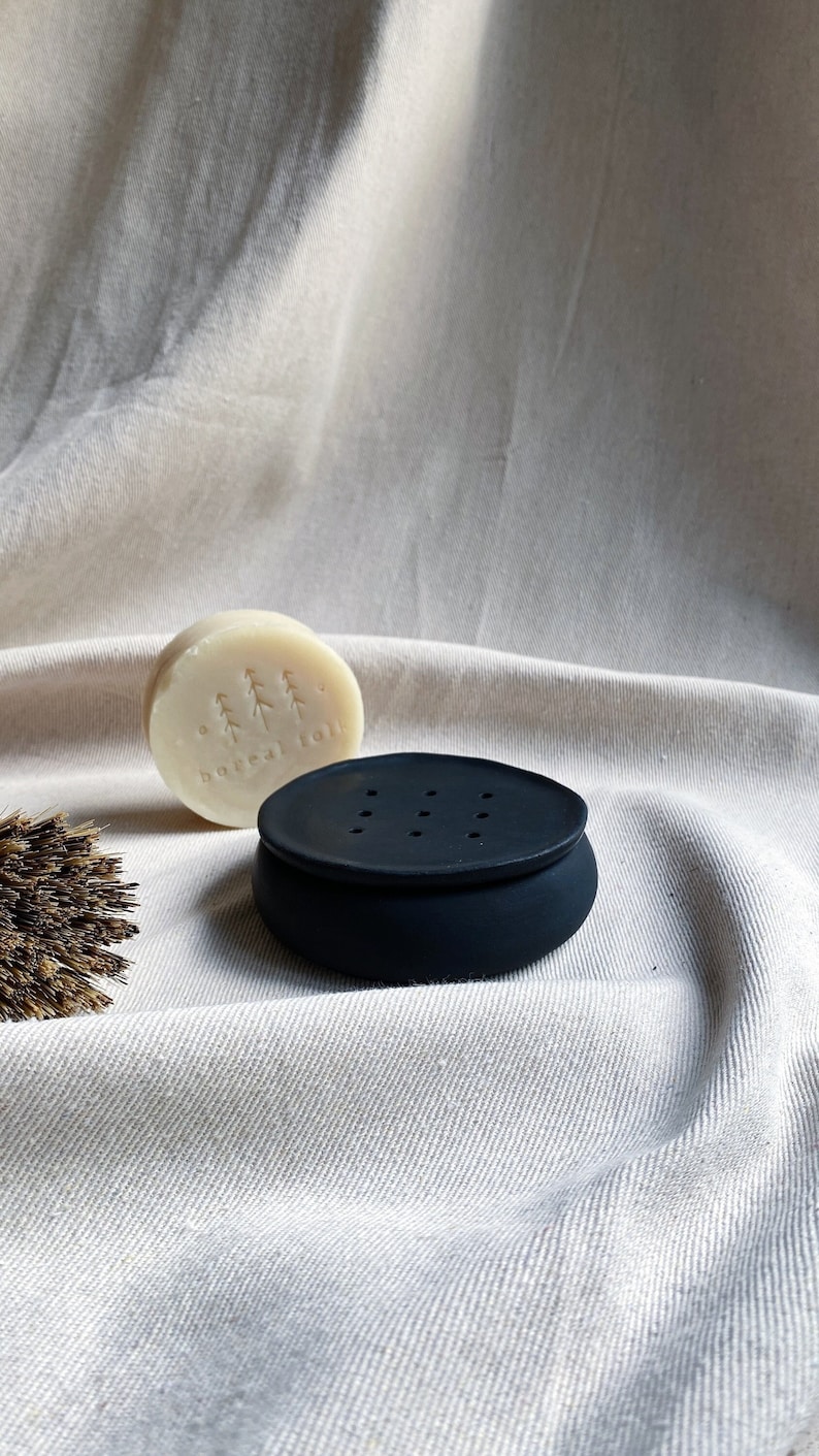 May include: A black soap dish with drainage holes and a white bar of soap with the text "boreal toil" on it.